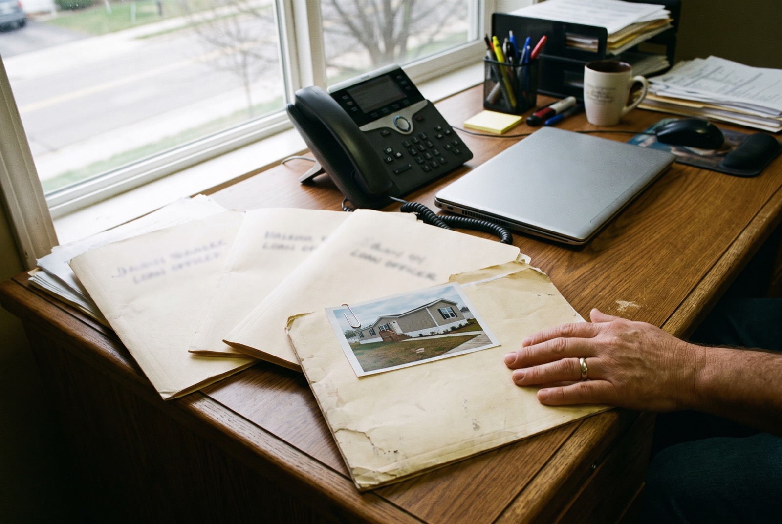A loan officer's desk with file folders, a phone and a photo of a manufactured home